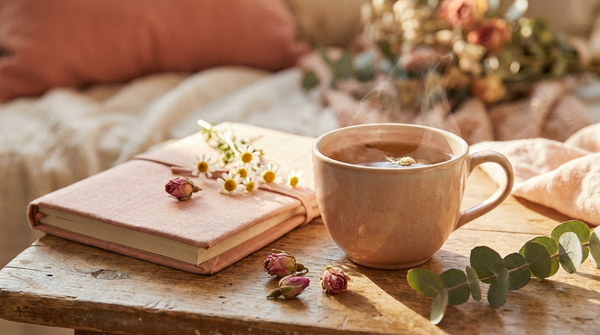 A calm still life of warm herbal tea, soft rose and botanical flowers and a linen journal in warm light